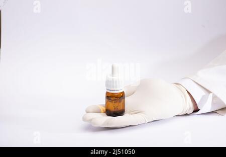 Marihuanaöl in Tropfenspender-Flasche in Handschuhen, weißer Hintergrund Stockfoto