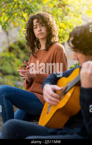 Junge lockige Frau, die mit einem Gitarristen auf der Straße singt Stockfoto