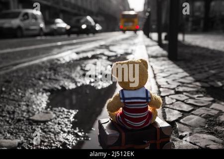 Kleiner Teddybär-Tourist in der Stadt sitzt auf seinem Koffer an der Bordwand und passt auf den verpassten Bus auf (Kopierplatz) Stockfoto