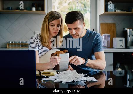 Mann und Frau überprüfen die Zahlungsrechnungen in der Küche zu Hause. Familienbudget planen. Paar berechnen Rechnungen und haben Stress Stockfoto
