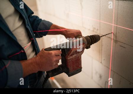 Nahaufnahme eines Handwerkers, der mit Hilfe eines Lasernivellers ein Loch mit Bohrer an der Wand machte Stockfoto