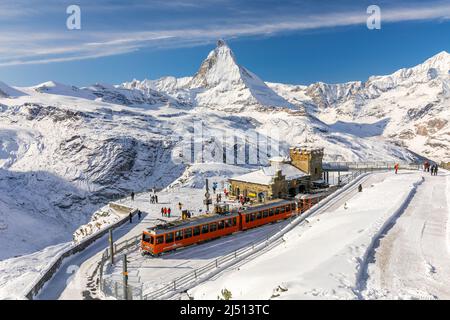 Gornergrat, Zermatt, Schweiz - 12. November 2019: Rote Seilbahn auf der Schneerbahn an der Bergstation mit Touristen und Matterhorn Summit in wi Stockfoto