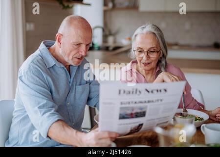 Glückliches Ehepaar, das zu Hause frühstücken und die Zeitung lesen kann. Stockfoto