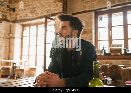 Nahaufnahme eines hübschen jungen Mannes, der in einem Café sitzt und wegschaut. Er wartet auf wichtige Neuigkeiten. Stockfoto