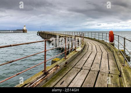 Der alte hölzerne Südpier am Eingang zum Hafen von Blyth in Northumberland, mit dem hübschen Leuchtturm am Nordpier in der Ferne. Stockfoto