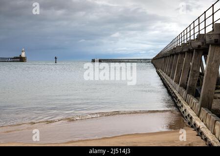 Die zwei alten hölzernen Pfeiler, die den Eingang zum Hafen von Blyth in Northumberland schützen, mit dem hübschen Leuchtturm am Nordpier in der Ferne. Stockfoto