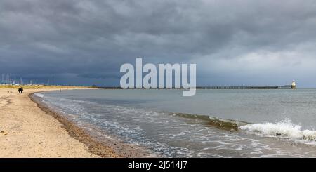 Der lange Sandstrand von Blyth ist bei Hundespaziergängern beliebt und bietet kilometerlange Sandstrände. Der Südpier am Hafen von Blyth liegt in der Ferne. Stockfoto