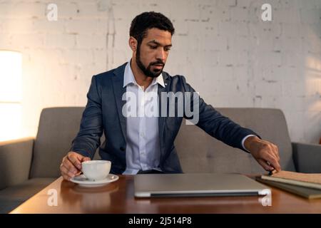 Beschäftigter junger Geschäftsmann, der Kaffee trinken und seine Arbeit erledigen kann. Stockfoto