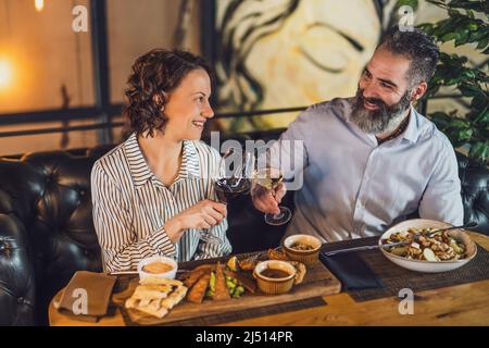 Glückliches Paar sitzt im Restaurant. Sie essen zu Abend mit Wein und verbringen eine schöne Zeit zusammen. Stockfoto