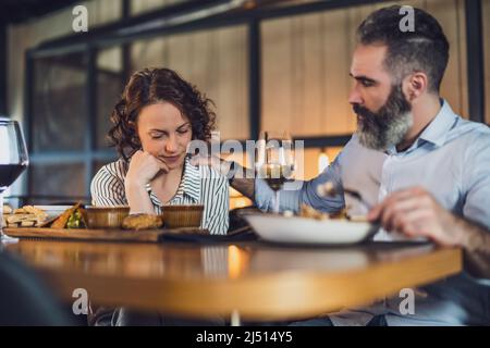 Ein erwachsenes Paar sitzt im Restaurant. Sie essen zu Abend mit Wein. Die Frau ist traurig und deprimiert. Stockfoto