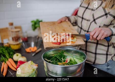 Frau wirft Gemüseschnitzel in einen Komposteimer in der Küche. Stockfoto