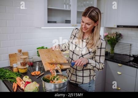 Frau wirft Gemüseschnitzel in einen Komposteimer in der Küche. Stockfoto