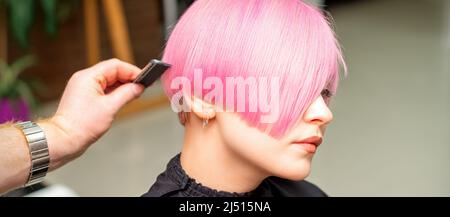 In einem Friseursalon kämmt ein Friseur die gefärbten, rosa Kurzhaar der Kundin Stockfoto