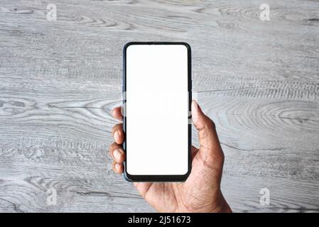 Hand hält Smartphone mit leeren weißen Bildschirm auf Holztisch Hintergrund. Stockfoto