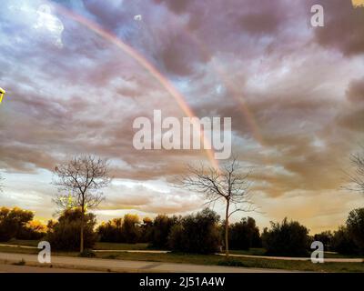 Regenbogen. Farbenfroher Regenbogen am Himmel von Valdemoro bei Sonnenuntergang, der den Regen mit der Sonne zusammenfällt. Wolkiger Himmel. Horizontale Fotografie. Stockfoto