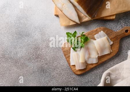 Köstliche geräucherte Heilbutt-Scheiben servierten Petersilie auf Holzschneidplatte auf grauem Hintergrund. Blick von oben. Speicherplatz kopieren. Stockfoto