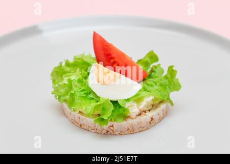 Reiskuchen-Sandwich mit Tomaten, Salat und Ei auf weißem Teller. Einfaches Frühstück. Diät-Essen. Schnelle und gesunde Sandwiches. Knäckebrot mit leckerer Füllung. Gesunder Ernährungs-Snack Stockfoto
