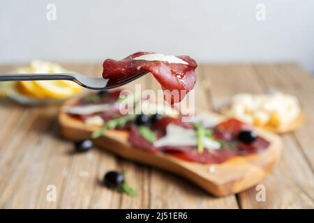 Jerky Fleisch bresaola auf der Gabel mit Zitronen, Grana, Oliven und Rucola Stockfoto