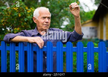 Alter Mann zeigt Faust im Freien neben dem Zaun Stockfoto