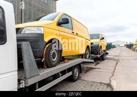 Weißer kleiner LKW-Autotransporter, beladen mit zwei gelben Minibussen auf einer Pritschenplattform und einem Sattelschlepper auf einer Straße am Straßenrand. Ehrenamtlich Stockfoto