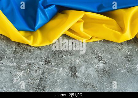 Ukrainische Satin-Flagge. Winkende Stofftextur Flagge der Ukraine. Echte Flagge auf betongrauem Hintergrund Stockfoto