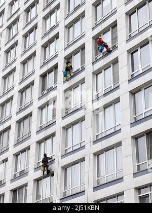 Industriekletterer waschen Fenster auf einem riesigen Wohngebäude. Das Arbeiten in der Höhe erfordert Fähigkeiten und Fertigkeiten. Stockfoto