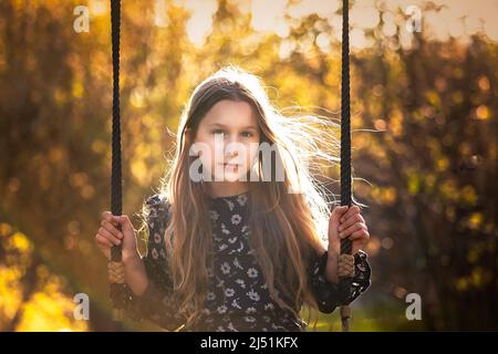 Schöne junge Mädchen, Kind, ältere Kind preteen sitzen auf einer Schaukel während der goldenen Stunde, Sonnenuntergang an einem Sommertag. Lange Haare, süß, herrlich, nachdenklich Stockfoto