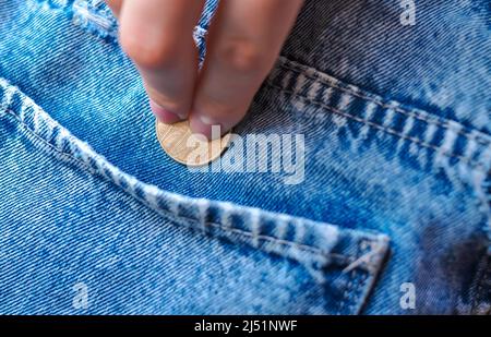 Hand legt Goldmünze Wechsel in Jeans Tasche Geld Konzept Stockfoto