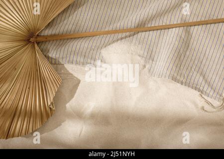 Getrocknetes Palmblatt und Strandtuch aus Leinen am Sandstrand mit Schatten von Palmen. Entspannung und tropisches Sommerferienkonzept Stockfoto