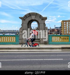 Mann auf einem Santander mietet sich ein Fahrrad, das über die Southwalk Bridge, London, Großbritannien, im April fährt Stockfoto