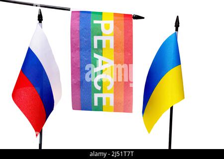 Nahaufnahme von russischen und ukrainischen Flaggen auf Fahnenmasten und zwischen ihnen, die von oben auf einer Regenbogenfahne mit dem Wort Frieden auf weißem Hintergrund A hängen Stockfoto
