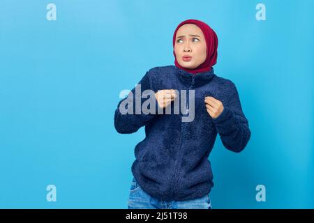 Porträt einer jungen asiatischen Frau, die sich heiß fühlt, trägt eine dicke Jacke auf blauem Hintergrund Stockfoto