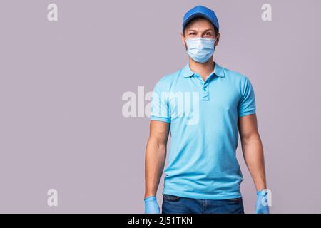 Junger Mann in blauer Uniform mit einer Schutzmaske und isolierten Handschuhen auf grauem Hintergrund Stockfoto
