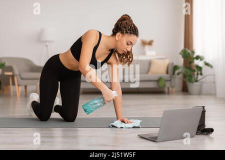 Schwarze Weibliche Reinigung Gymnastikmatte Mit Waschmittel Vor Dem Training Im Innen Stockfoto