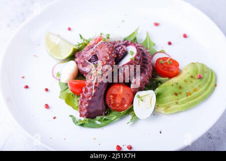 Warmer Salat mit Oktopus, Kirschtomaten, Avocado, Rucola, Wachteleiern, Rettich und Kalk auf einem weißen Teller. Traditionelle mediterrane Gerichte. Nahaufnahme. Stockfoto