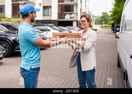 Ein professioneller Mann mit blauer Uniform liefert einer Kundin Pizza Stockfoto