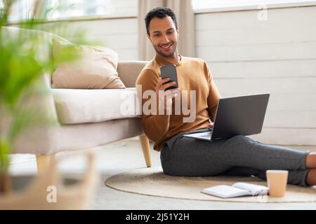 Porträt eines Mannes, der zu Hause Smartphone und pc verwendet Stockfoto