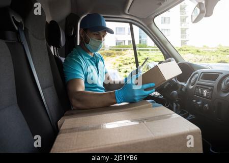 Ein junger Kurier in einem Lieferwagen überprüft vor der Auslieferung Pakete und Frachtbriefe mit einem Tablet-pc Stockfoto