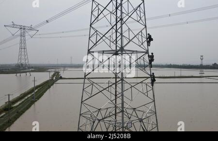 (220419) -- HEFEI, 19. April 2022 (Xinhua) -- Luftfoto vom 19. April 2022 zeigt Arbeiter, die den Stromübertragungsturm besteigen, um das 500-Kilovolt-Gleichstrom-Übertragungsprojekt „Longquan-Zhengping“ im Landkreis Lujiang in Hefei, der ostchinesischen Provinz Anhui, zu unterhalten. In Lujiang in der ostchinesischen Provinz Anhui arbeitet ein Team von Versorgungstechnikern wie „Spidermen“ an der Wartung des 500-Kilovolt-Gleichstromanübertragungsprojekts, das von Longquan nach Zhengping expandiert. Die Stromleitung, die Anhui durchläuft, ist einer der wichtigsten Kanäle, die über 10 Milliarden kWh Strom pro Jahr übertragen. Stockfoto