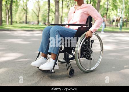 Beschnittene Ansicht einer jungen afroamerikanischen Frau, die im Rollstuhl im Freien sitzt, Nahaufnahme Stockfoto