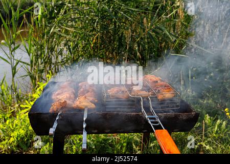 Hähnchenspieße werden auf Spießen und einem gegrillten Rost gebraten Stockfoto