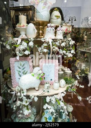 Kunstvolle Osterdekoration, Einrichtung und Souvenirs auf Glasvitrine mit weißen Keramikeiern, Glocken und Blumen. Stockfoto