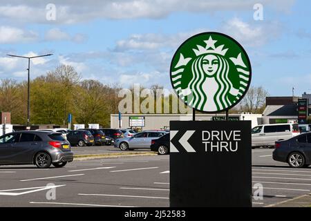 Swindon, England - April 2022: Schild auf dem Parkplatz einer Tankstelle auf der Autobahn M4, das eine Drive-Thru-Filiale von Starbucks anwirbt Stockfoto