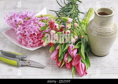 Floristin bei der Arbeit: Frau zeigt, wie man Frühlingsstrauß mit Tulpe, Hyazinthe und Nelkenblumen zu machen. Schritt für Schritt, Tutorial. Stockfoto