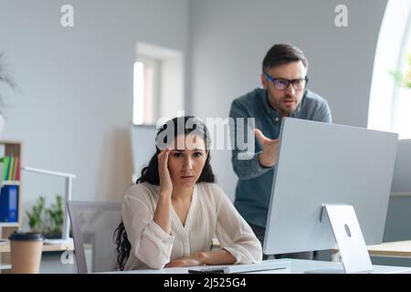 Unglückliche junge Mitarbeiterin, die Fehler im Projekt machte, die Frist versämte, von ihrem Chef im Büro beschimpft wurde Stockfoto