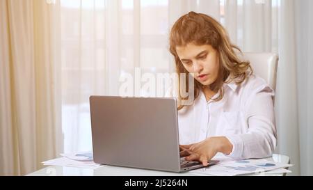 Eine behinderte Freiberuflerin arbeitet von zu Hause aus am Tisch auf einem Laptop Stockfoto