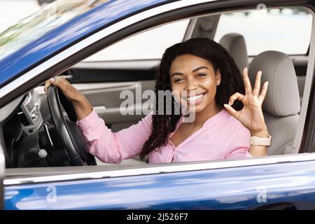 Glückliche schwarze Frau, die im Auto sitzt, zeigt eine gute Geste Stockfoto