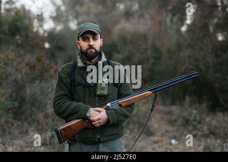 Selbstbewusster Mann mit Gewehr in Wäldern während der Jagd Stockfoto