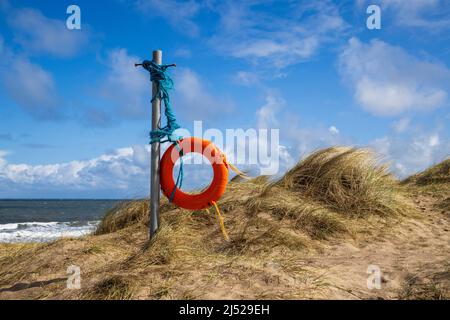 Eine gebrettete Life Boje, die in der Meeresbrise in den Sanddünen der Embleton Bay, Northumberland Coast, England, weht Stockfoto