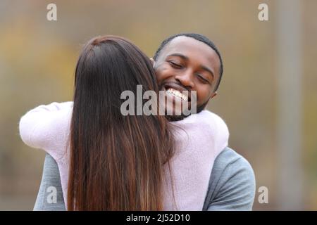 Vorderansicht Porträt eines glücklichen Mannes mit schwarzer Haut umarmt einen Freund draußen Stockfoto